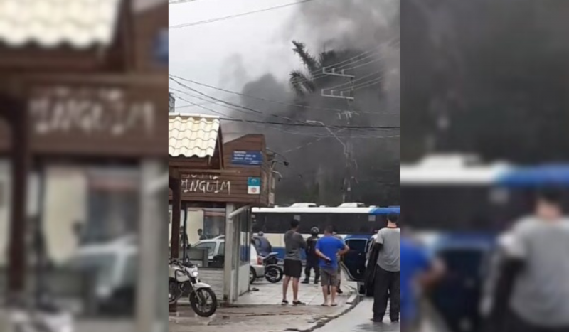 Foto mostra moradores vendo muita fumaça em função de um protesto feito na rua. Imagem também mostra um ônibus atravessado na pista.