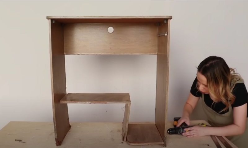 Decoradora usa furadeira na base do móvel velho no processo de transformação