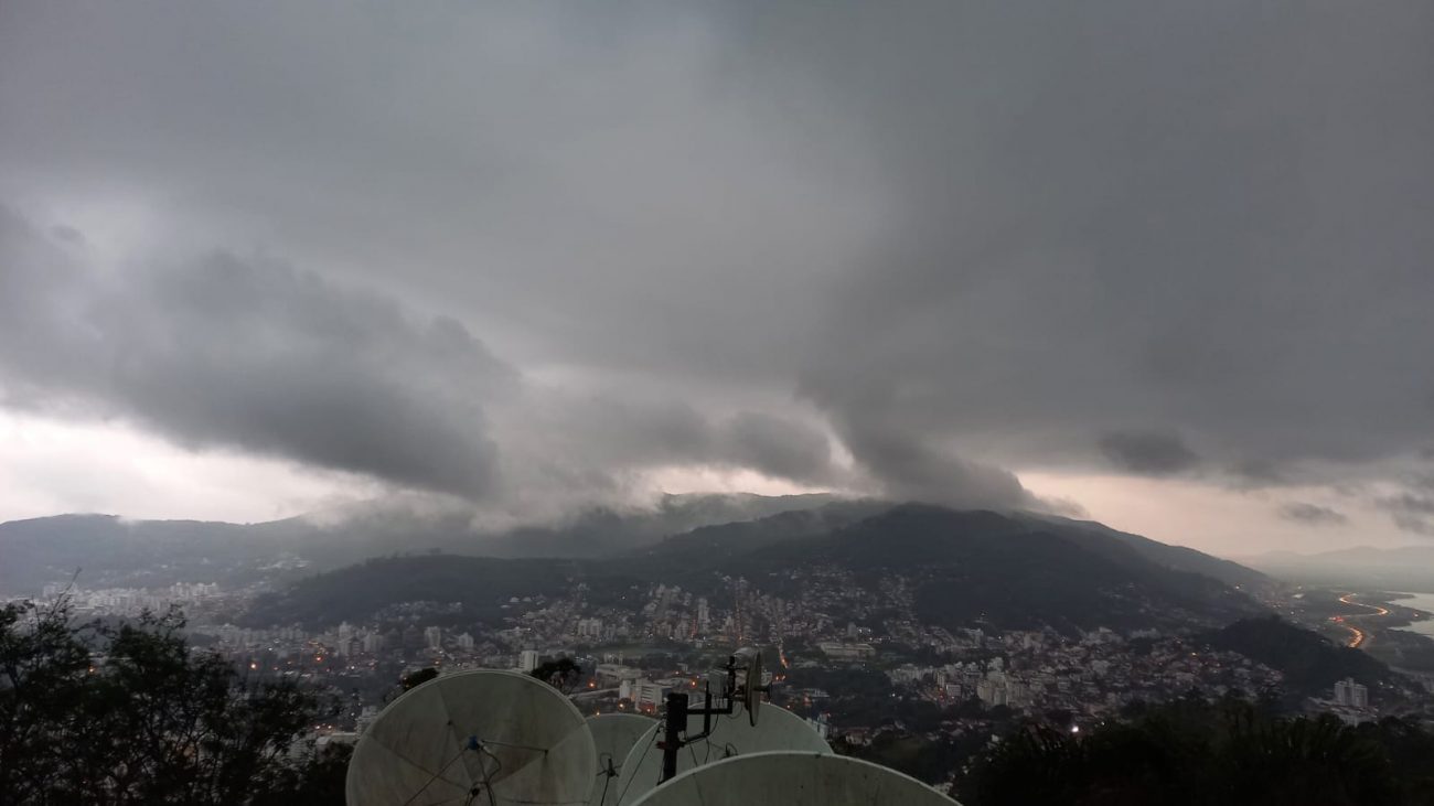 Na foto aparece um topo de nuvens carregadas de chuva tocando uma montanha em Florianópolis.