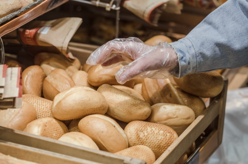 Foto de uma mão segurando um pão de trigo sendo retirado de uma cesta na padaria