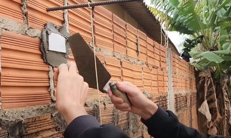 Pedreiro fixa peça na parede de tijolo que vai servir como guia para aprumar o muro