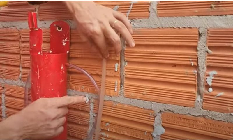 Pedreiro confere o nível com o aparelho que criou fixando a mangueira na parede de tijolo