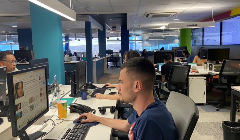 Pessoas trabalhando em computadores dentro de uma redação do portal ND+