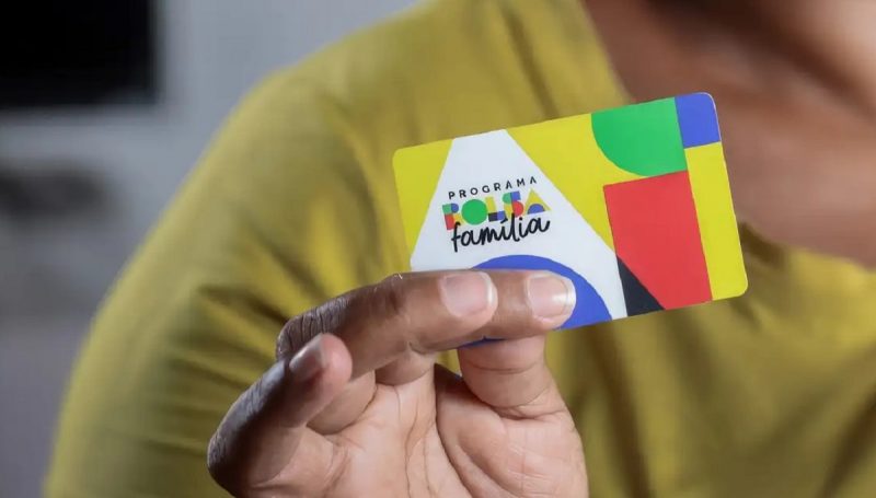 Mão segurando cartão colorido do Bolsa Família