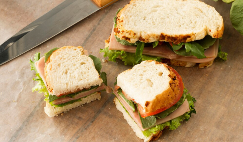 Na foto é possível ver três sanduíches, um grande e dois pequenos, todos com queijo, presunto, alface e tomate dentro.