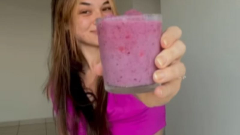 Mulher segurando smoothie roxo de morango em copo de vidro