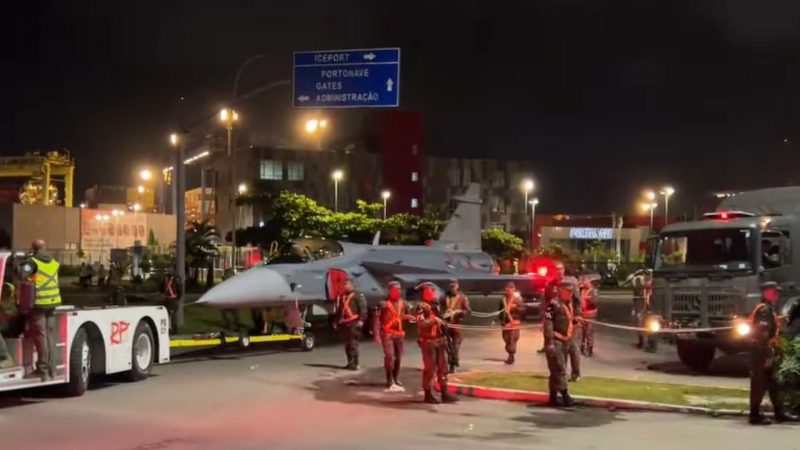 Caça Gripen sendo transportado por agente do exército, polícia militar e força aérea brasileira