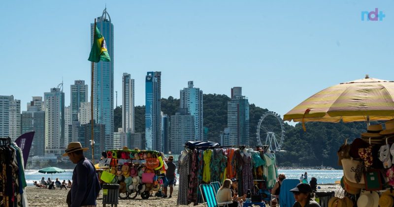 Foto mostra praia Central de Balneário Camboriú com ambulantes e turistas