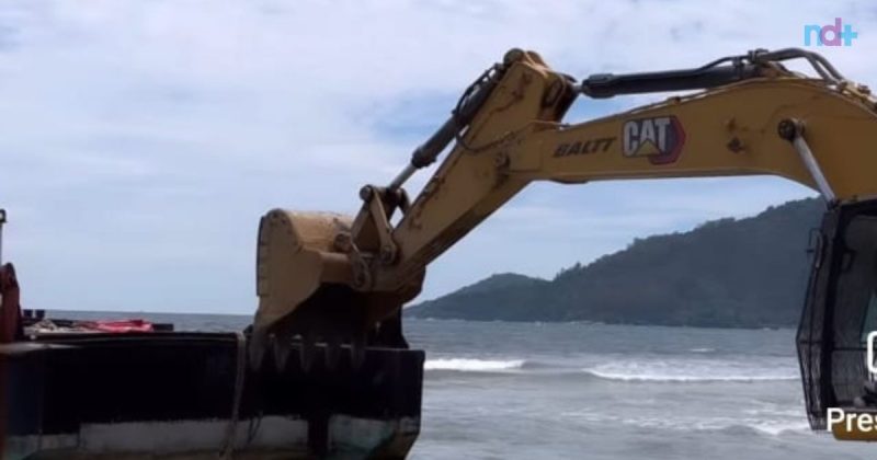 Na imagem é possível ver retroescavadeira empurrando barcaça na praia Central de Balneário Camboriú