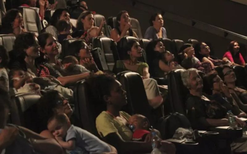 Mães reunidas em uma sessão de cinema do CineMaterna, muitas carregando seus bebês