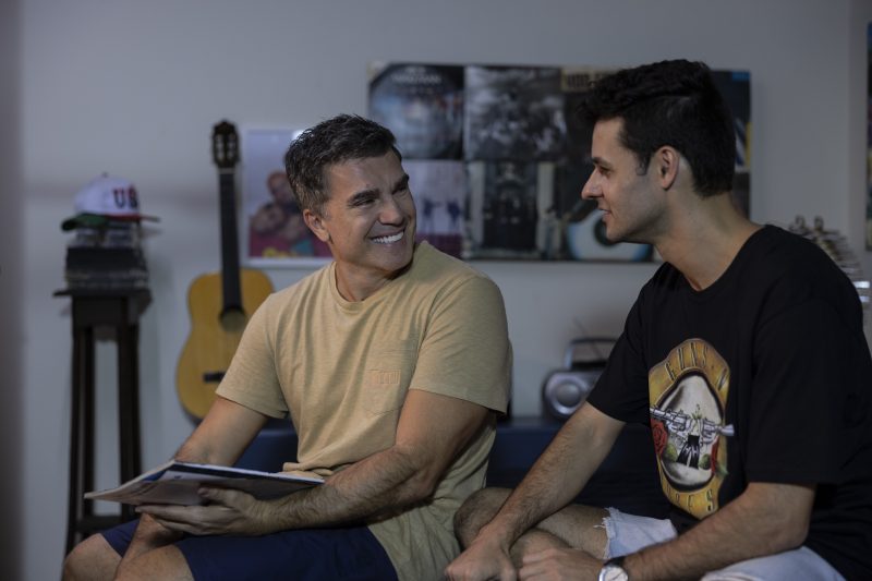 Foto mostra Dinho e o pai sentados com uma revista na mão