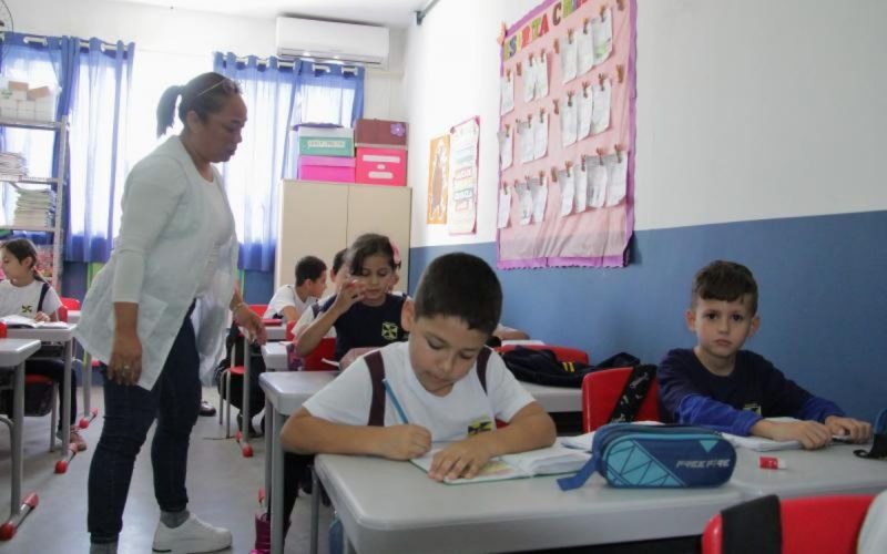 Alunos das escolas municipais de Itajaí em sala de aula, com professora os auxiliando