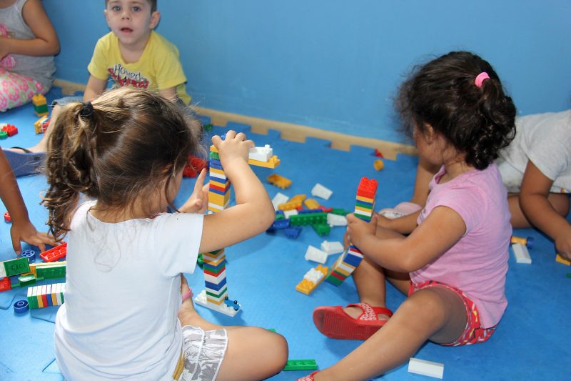 Crianças brincando com lego no chão de creche; imagem representa programa Fila Única