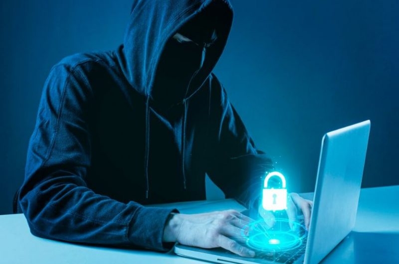 Illustrative image of a hooded hacker trying to hack and bypass the security of a laptop