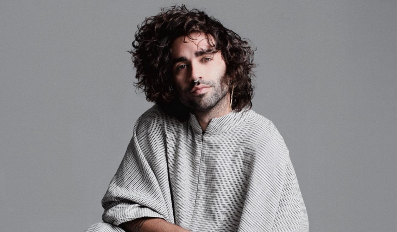 Hóttmar Loch, catarinense na Forbes Under 30 em 2023 - Na foto, homem branco, de barba e cabelos tamanho médio na cor castanho escuro, posa usando blusa cinza quadriculada em frente a fundo cinza.