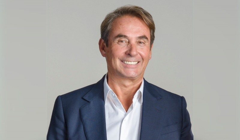 Bilionário magnata de SC sorrindo usando blusa social branca e terno azul