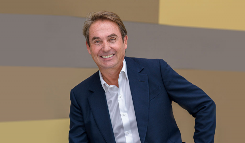 Foto mostra o magnata de SC, Jaimes Almeida Junior, sorrindo, sentado usando blusa branca social e terno azul escuro