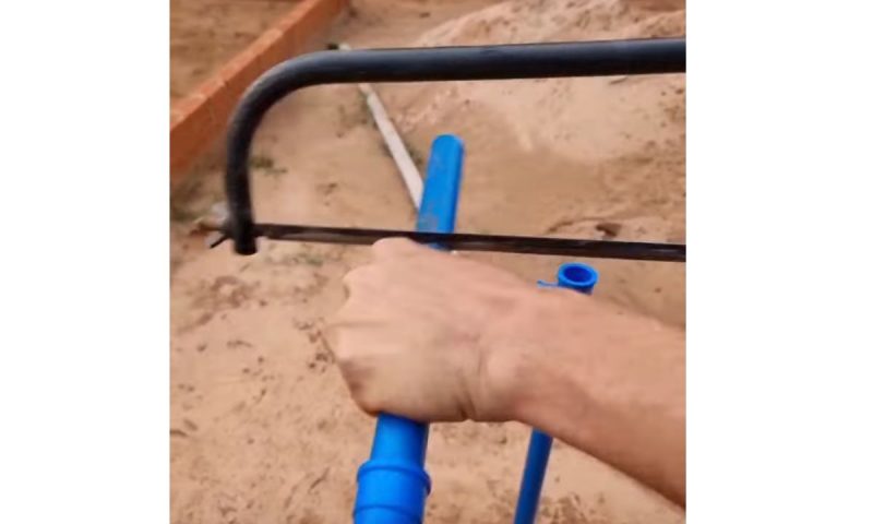 Pedreiro serra pedaço de cano para construir engenho que faz filete virar jato de água