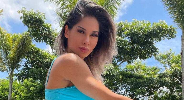 Maíra Cardi com roupa azul, na frente de árvore verde