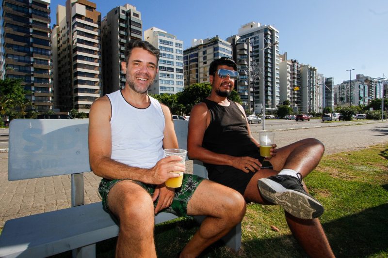 Dois homens de meia idade sentados em um banco no calçadão da avenida Beira-Mar Norte, tomando caldo de cana