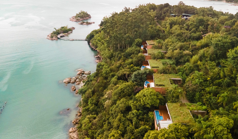 Na foto é possível ver à direita uma espécie de ilha, com muita vegetação e algumas cabanas com piscina. E à esquerda, o mar na cor verde água