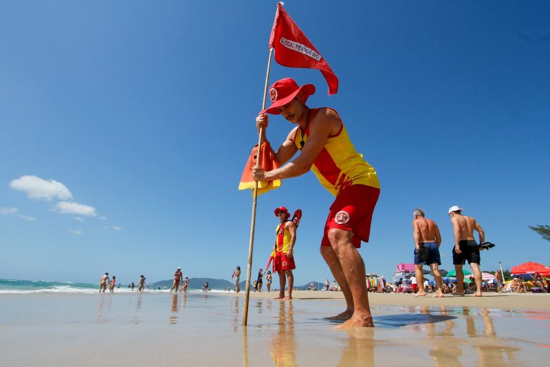 Bombeiro fincando uma bandeira de local perigoso em areia de praia de Florianópolis