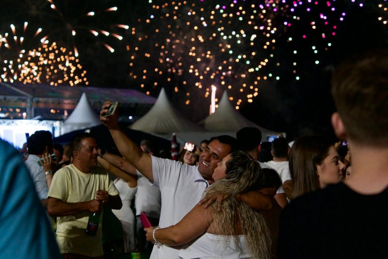 Foto mostra casal tirando foto com fogos ao fundo para ilustrar matéria sobre quanto custa passar o Réveillon em Balneário Camboriú