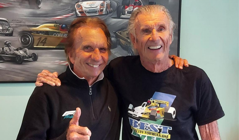 Emerson Fittipaldi (à esquerda) e Wilson Fittipaldi (a direita) - Na foto, dois homens brancos e idosos posam usando roupa preta e sorrindo juntos 