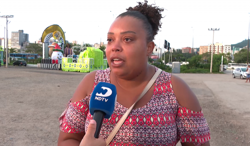 Na foto, mulher negra, usa blusa de estampa étnica e bolsa a tira colo, fala em frente a microfone