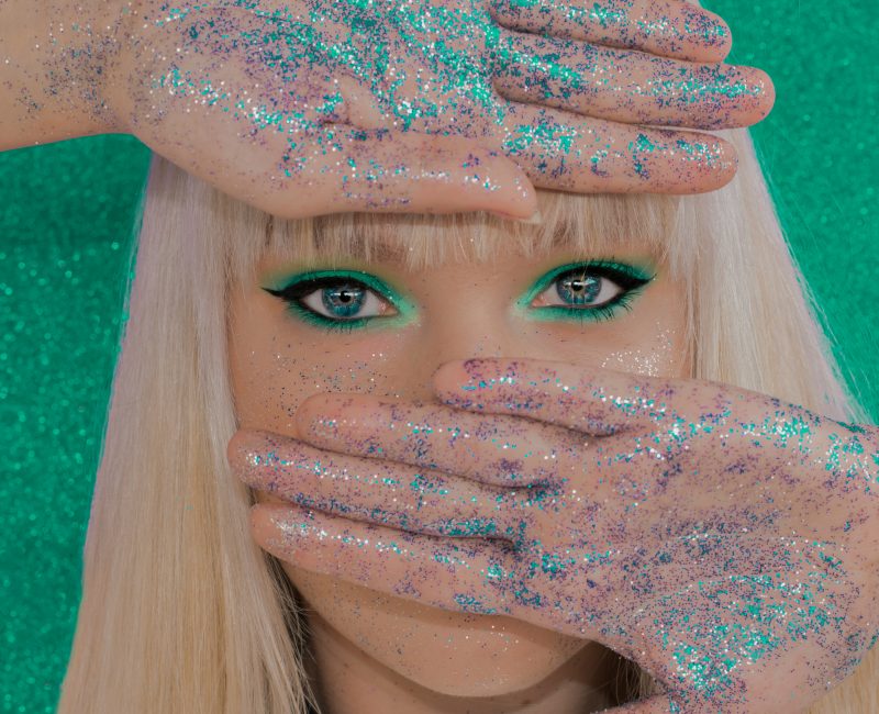Foto mostra rosto de mulher com as mãos cheias de glitter