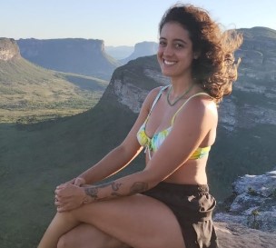 Foto de Lindalva Firme Guedes sentada de pernas cruzadas em um morro com paisagem bucólica