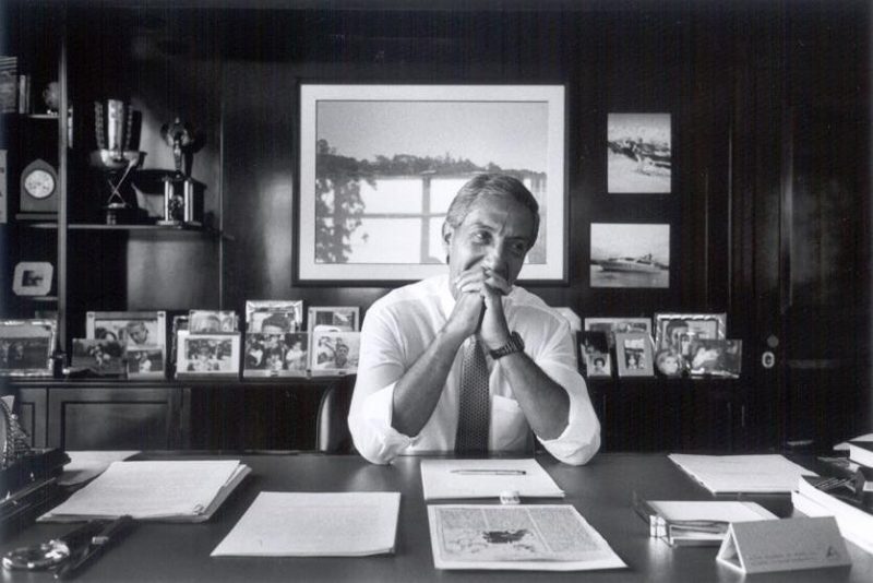 Foto mostra Abilio Diniz sentado em uma mesa em seu escritório com as mãos cruzadas na frente do rosto