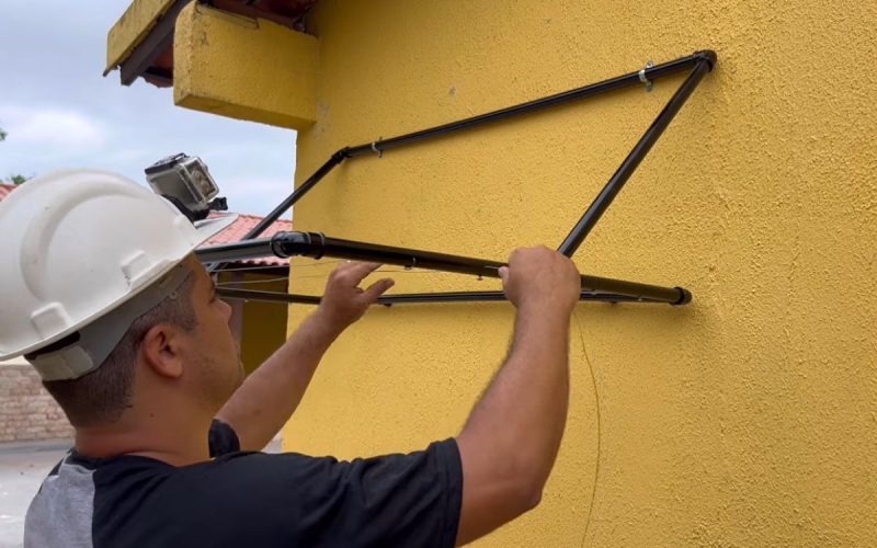 Frame de vídeo em que um pedreiro ensina a fabricar um varal retrátil feito com tubos PVC