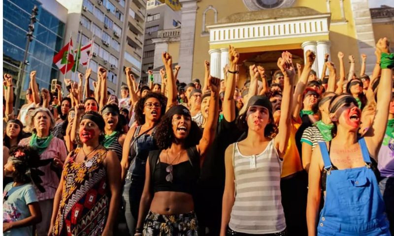 Foto mostra centenas de mulheres com as mãos para cima durante a marcha do Dia Internacional da Mulher