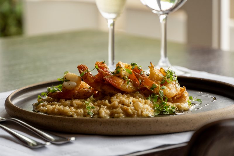 Imagem de um prato de risoto de frutos do mar acompanhado de taça de vinho 