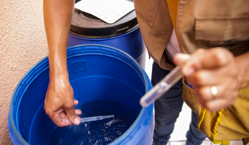 Pessoas segurando tubos para coletar água de dentro de balde azul escuro