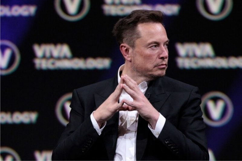 foto mostra Elon Musk olhando para o lado sério com os dados das mãos unidos