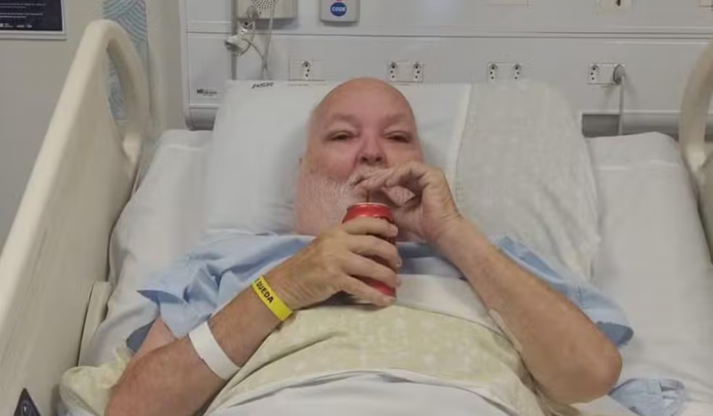 Homem idoso branco deitado em leito de hospital tomando coca cola no canudinho