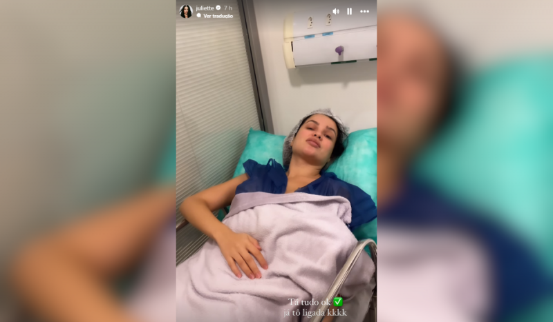 Foto mostra mulher com roupa hospitalar e touca, deitada em uma maca, coberta por um lençol lilás