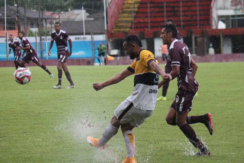 Jogador do Criciúma chuta a bola enquanto a água levanta