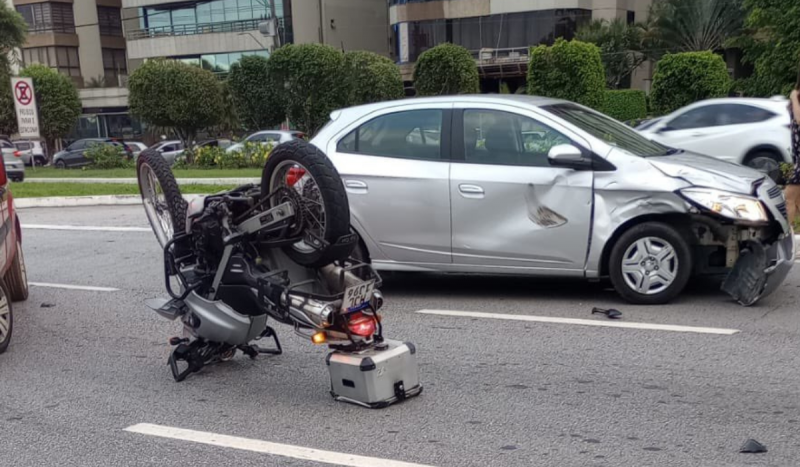 Motocicleta virada de cabeça para baixo no meio da rua após acidente. Imagem também mostra carro cinza com a parte dianteira amassada