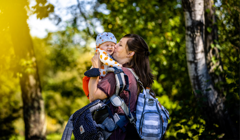Mulher beijando no rosto de bebê enquanto ele sorri, para ilustrar matéria sobre o perigo do beijo em crianças