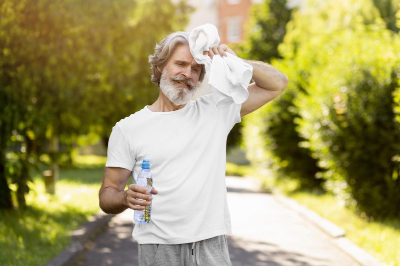 Homem caminhando com uma garrafa de água, secando o suor em um dia quente