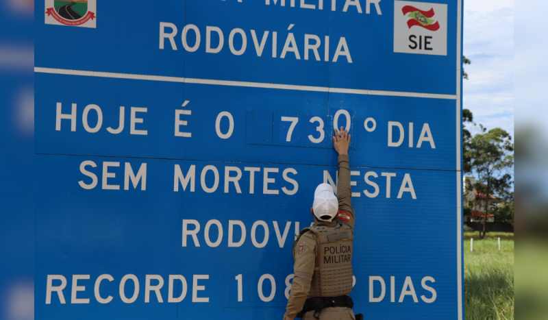 Policial mudando número em placa azul que conta acidentes em rodovia