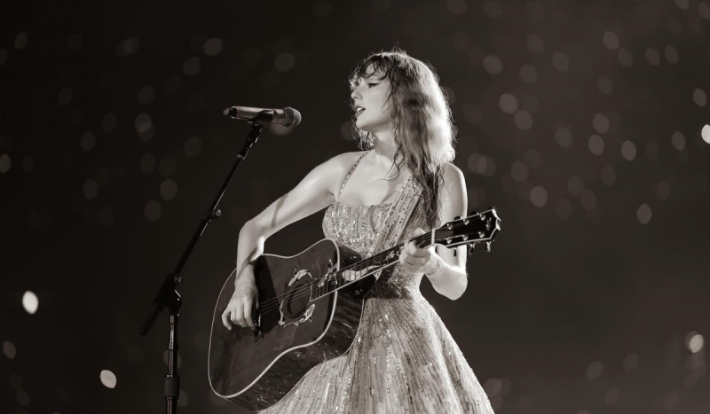 Taylor Swift cantando - Foto mostra mulher branca com vestido brilhoso tocando violão. Foto está em preto e branco