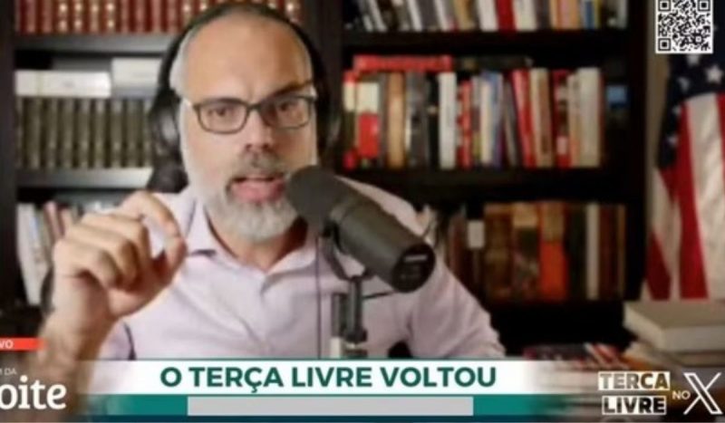 foto mostra um print da live de Allan dos Santos, onde ele aparece com fones de ouvidos e falando em um microfone com um fundo de blblioteca, a imagem também tem uma tarja escrito "o terça livre voltou"