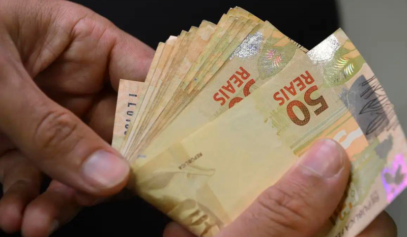 Pessoa contando notas de 50 reais na mão para ilustrar matéria sobre o rendimento com o aluguel em Santa Catarina