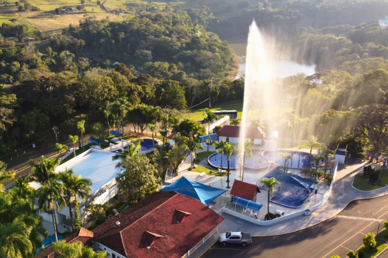 Foto aérea do Parque Termas de Piratuba. Na imagem, aparecem várias piscinas e um enorme chafariz que esguicha água bem alto. A estrutura é toda cercada por árvores e vegetação.