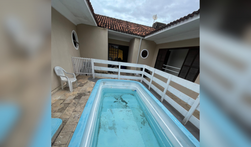 Foto mostra área externa de residência com piscina azul cheia pela metade, e sujeiras no fundo da piscina