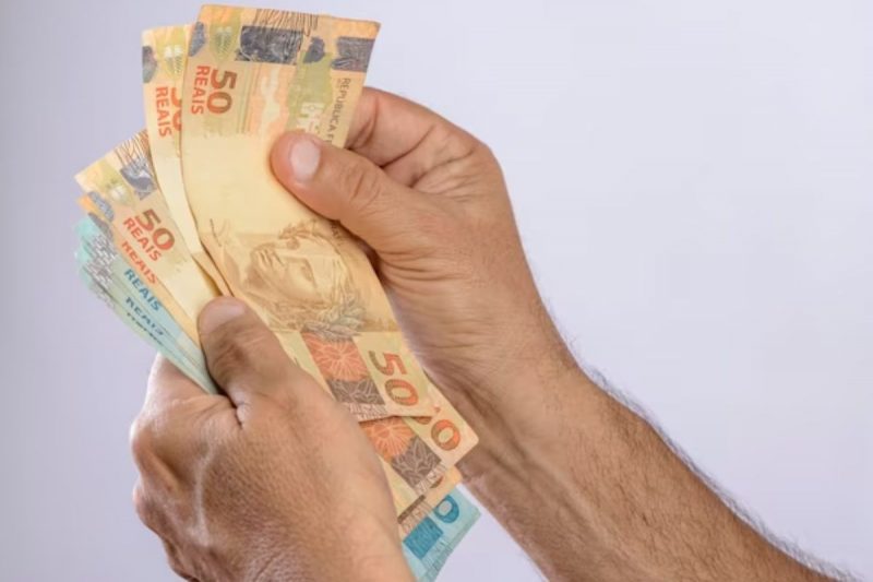 mão segura notas de R$ 50 e R$ 100 para exemplificar R$ 138 milhões vão ser liberados para saque a partir de 8 de maio